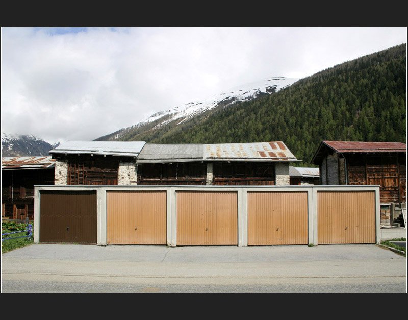 Unsere heutige Zeit, gesehen in Obergesteln im Wallis. Normalerweise kein Motiv, das zum Fotografieren anregt. Hier fand ich die  unpassende  Situation bemerkenswert, diese ungestaltete Kiste im Gegensatz zu den historischen Vorratsh�usern, die teilweise zu Wohnh�usern umgebaut wurden. Witzig: das eine dunkelbraune Tor. (Matthias)